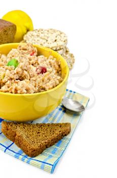 Porridge rye flakes with candied fruit in a yellow cup, dark rye bread, spoon on a napkin, quince and round cereal bread isolated on white background