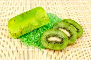 Green homemade soft soap and salt, three slices of kiwi on a bamboo napkin