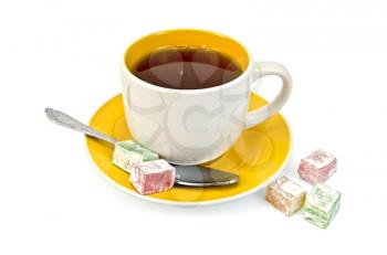 Tea in yellow cup, a spoon, a few pieces of colored lokum isolated on white background