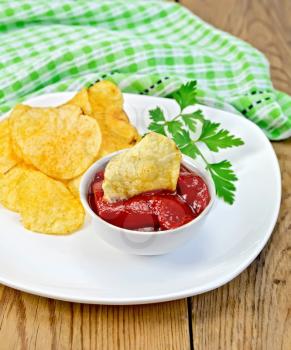A plate of potato chips, a bowl with tomato ketchup and chips, green cloth background of wooden board
