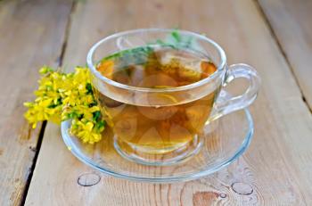 Tea in a glass cup, fresh flowers tutsan against a wooden board