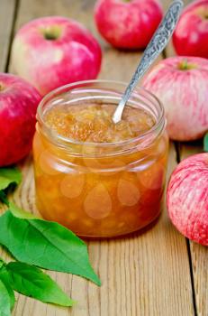Apple jam in a glass jar with a spoon, fresh red apples, twigs with leaves on a wooden board