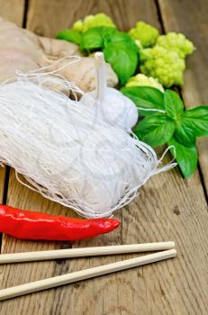 Thin rice noodles with garlic, hot red pepper, ginger, basil and broccoli, chopsticks on a background of wooden boards