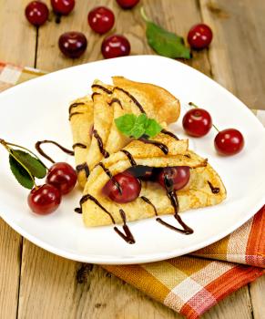 Two pancakes with berries cherries, mint, chocolate icing on a white plate with a napkin on a wooden boards background