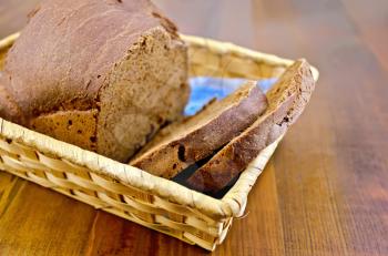 A loaf of sliced rye slices of homemade bread in a wicker basket on a wooden boards background