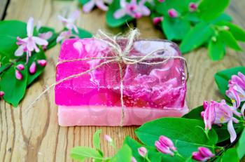Two bars of soap homemade pink, tied with twine, twigs with leaves and pink flowers of honeysuckle on a background of wooden boards