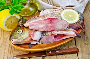 Bream whole peeled and cut into chunks in a clay plate, parsley, lemon, vegetable oil, napkin, knife on the background of wooden boards