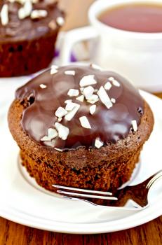 Chocolate cupcake, fork on a white plate, cupcake on a napkin, tea in the cup on the background of wooden boards