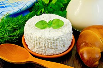 Curd in a clay pot with basil, a wooden spoon, bagel, dill, parsley, a jug of milk, a napkin on a wooden board
