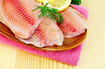 Tilapia fillets with lemon and dill in a pottery on a pink napkin on the background of wooden boards