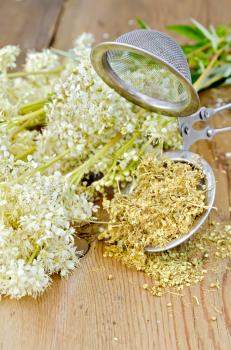Metal strainer with dried flowers of meadowsweet, a bouquet of fresh flowers of meadowsweet against a wooden board