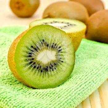 Whole and half kiwi, green napkin on a wooden board