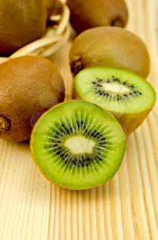 Whole and half kiwi fruit in a wicker plate on a wooden board