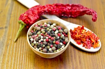 Pepper peas in a wooden bowl, flakes of red pepper in a wooden spoon, a pod of red pepper against a wooden board