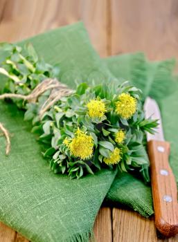 Rhodiola rosea flowers, tied with string with a knife on a green napkin on a background of wooden boards