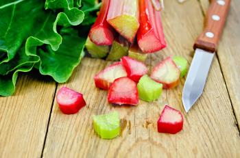 Bundle of stalks of rhubarb, cut pieces of rhubarb with a leaf and a knife on a wooden board