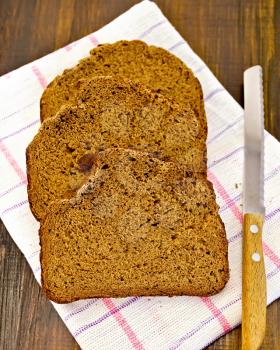 Three slices of homemade rye bread on a napkin with a knife on a wooden boards background
