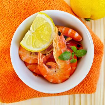 Raw shrimp in a white bowl with lemon and basil on a orange napkin and a wooden board