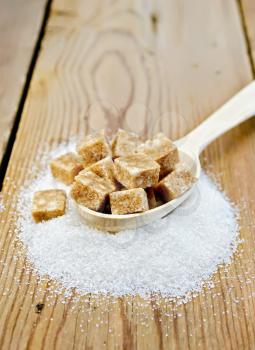 Cubes of brown sugar in a wooden spoon and a white granulated sugar on a wooden table