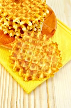 Round golden waffles on a plate and a yellow napkin on a background of wooden board