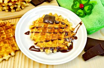 Round waffle with chocolate sauce, bauble in the shape of a flower with a ladybug, slices of chocolate, green napkin on a wooden board