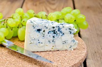 Blue cheese, grapes, knife on background wooden board
