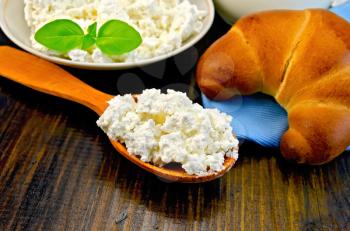 Cottage cheese in a saucer with basil on a wooden spoon, a bagel, a pitcher of milk, napkin on wooden board