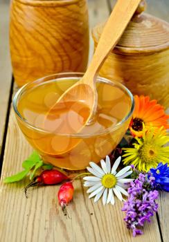 Honey in a glass bowl and wooden banks, spoon, berries of briar, flowers on the background of wooden boards