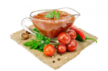 Ketchup in a glass sauceboat with tomatoes and parsley, hot pepper, garlic on a sacking isolated on a white background