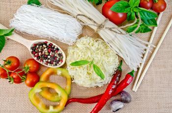 Rice noodles are different, tomatoes, peppers, chopsticks, garlic, basil on a background of sack cloth top