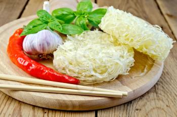 Stranded rice noodles with garlic, hot red pepper, ginger, basil, chopsticks on a wooden boards background