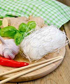 Thin rice noodles with garlic, hot red pepper, ginger, basil, napkin, chopsticks on a background of wooden boards