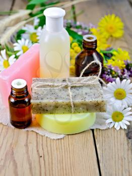 Oil and lotion bottles, homemade soap on a piece of paper, chamomile flowers, tansy, elecampane on the background of wooden boards