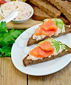 Sandwiches on two pieces of rye bread with cream, dill, cucumber and salmon in the oval plate on the background of wooden boards
