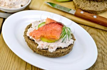 Sandwich of rye bread with cream, cucumber, dill and salmon on a plate on a wooden board