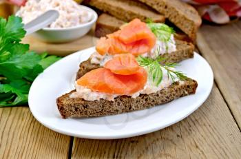 Sandwiches on two pieces of rye bread with cream, dill, cucumber and salmon in a white plate on a wooden boards background