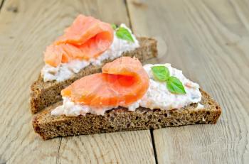 Toast two slices of rye bread with cream, basil and salmon on the background of wooden boards