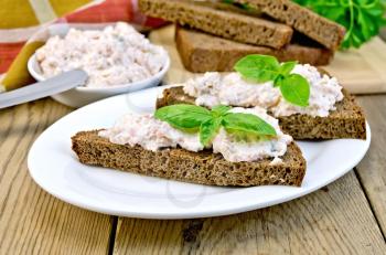 Toast two slices of rye bread with cream of salmon and mayonnaise, basil, knife, napkin, parsley on a wooden boards background