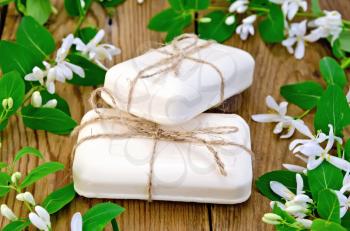 Two bars of soap white, tied with twine, twigs with leaves and white flowers of honeysuckle on a background of wooden boards
