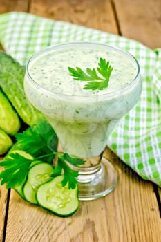 Yogurt in glass with cucumber, parsley, napkin against a wooden board