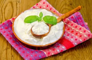 Thick yogurt in a clay bowl, basil, spoon, napkin against a wooden board