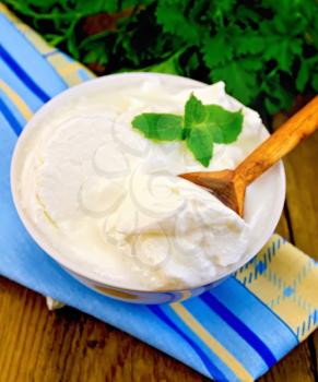 Thick yogurt and a wooden spoon in a white bowl, parsley, napkin, mint on the background of wooden boards