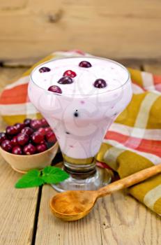 Thick yogurt in glass with cranberries, spoon, napkin, cranberries in a bowl, mint on a wooden boards background