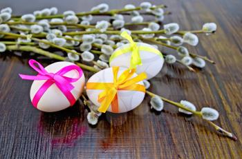 Three Easter eggs tied with colored ribbons, willow twigs on a wooden board