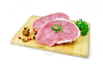 Two slices of pork, nutmeg, parsley, rosemary and pepper on a wooden board isolated on white background
