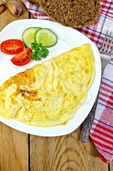 Omelette with slices of tomato, cucumber, parsley and fork on a plate, napkin, bread on a wooden boards background