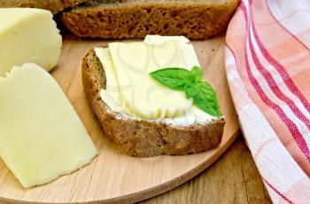 Sandwich on a slice of rye bread with butter and cheese, basil, napkin, on a background of wooden boards