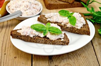 Sandwiches on two pieces of rye bread with cream of salmon and mayonnaise, basil, knife, napkin on the wooden boards
