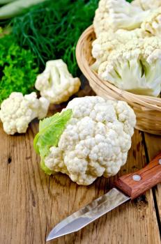 Cauliflower on a table and in a wicker basket, knife, dill, parsley, napkin on wooden board