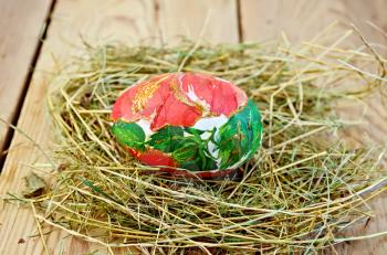 Easter egg with a pattern of red flowers and green leaves in the hay on the background of wooden boards